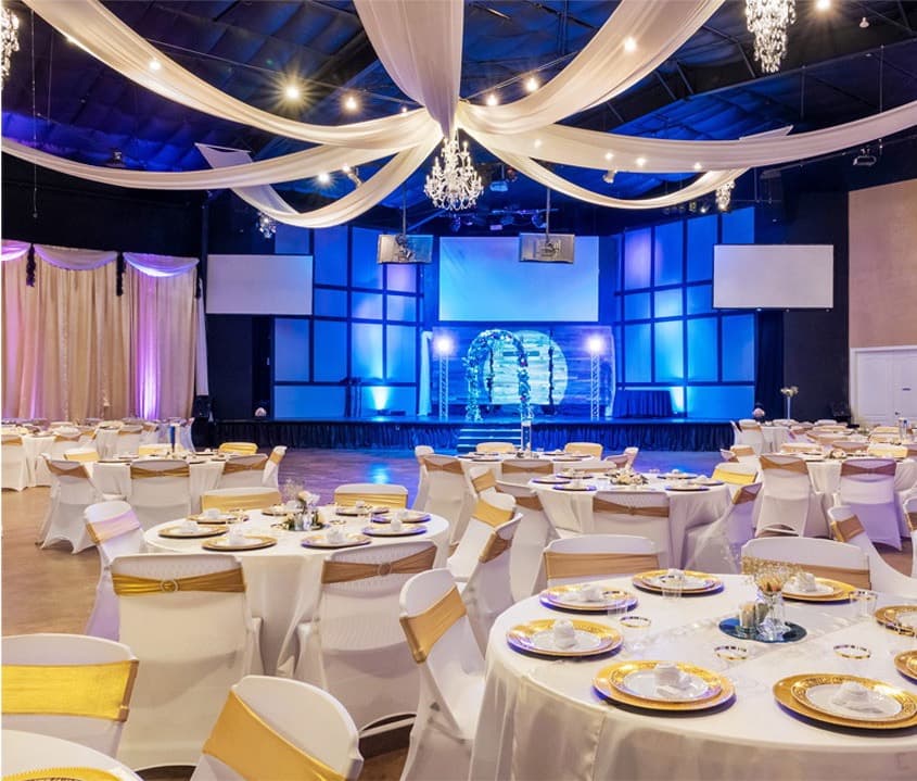 The Embassy Events ballroom set for a celebration with draped ceilings, chandeliers and gold chair sashes